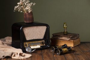 Gammal rörradio på ett träbord bredvid böcker, kikare och torkade blommor